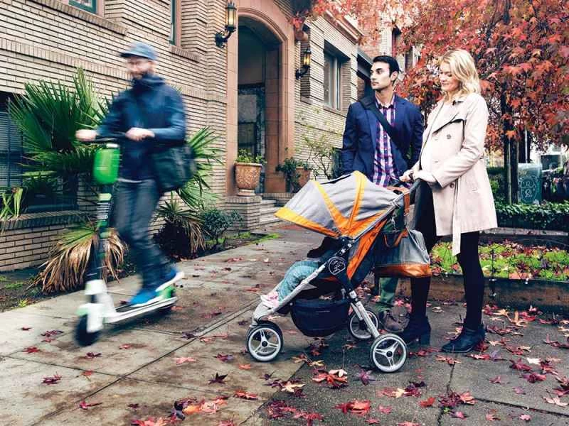 男性がスクーターに乗っている男性を見つめ、妻はベビーカーに乗っている赤ちゃんを見つめている